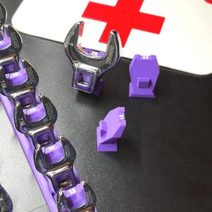 May include: A set of chrome wrenches with purple holders, labeled with sizes. The wrenches are arranged on a purple rack. The image also shows individual purple wrench holders and a sign that says TOOL DOC with a red cross.