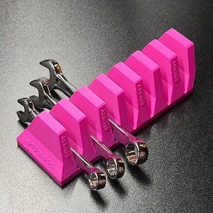 May include: A bright pink wrench organizer with the word "STUBBY" printed on the side. The organizer holds several silver wrenches. The word "Toolbox" is printed on the front of the organizer. The wrenches are arranged in ascending order.