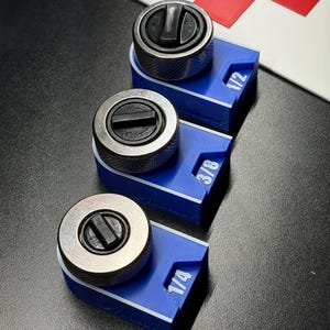 May include: Three metal ratchet heads with blue bases, labeled 1/4, 3/8, and 1/2. The ratchets have a silver finish and black controls. The bases are blue with white lettering. The background is black with a red and white cross.
