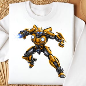 Può includere: Felpa bianca con un'illustrazione dettagliata di un personaggio robotico giallo e grigio con occhi blu e un'arma che spara un raggio di energia blu. Il robot è in una posa dinamica.