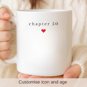 以下が含まれることがあります： 赤いハートの上に「chapter 50」の文字が書かれた白いセラミックマグカップ。クリーム色のセーターを着た人がマグカップを持っています。マグカップの底には「Customise icon and age」の文字があります。
