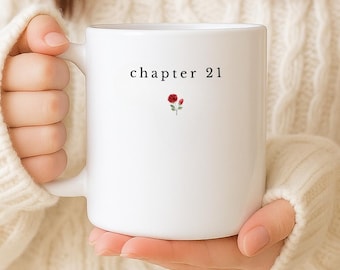 May include: White ceramic mug with the text "chapter 21" and a small red rose illustration. The mug is held by a person wearing a cream-colored sweater. The bottom of the image has the text "Customise Birth Flower and Age".