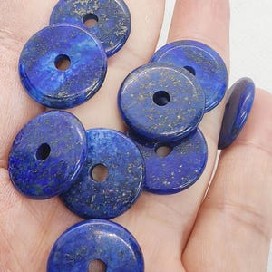 May include: A collection of deep blue, circular lapis lazuli beads with a central hole. The beads have a polished surface with flecks of gold and are of varying sizes. These gemstone beads are ideal for jewelry making.