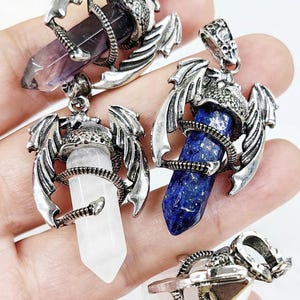 Puede incluir: Cuatro colgantes de piedras preciosas. Cada colgante presenta una punta de cristal sujeta por un dragón plateado. Los cristales son morados, azules, blancos y transparentes. Los colgantes tienen un lazo para una cadena.