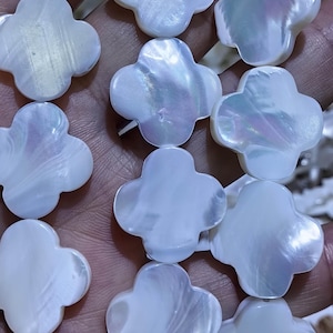 May include: Close-up of a strand of white, four-leaf clover-shaped beads. The beads have a pearlescent sheen, reflecting light with hints of blue and purple. These beads are ideal for jewelry making.