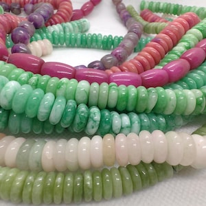 Può includere: Una collezione di collane di perline in vari colori, tra cui tonalità di verde, rosa e viola. Le perline sono rotonde e piatte, creando un effetto a strati. Le collane sono disposte in un mucchio, mostrando i diversi colori e le trame.