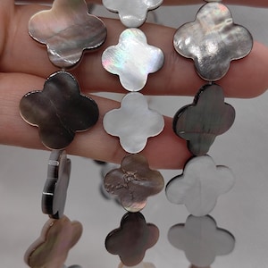 May include: Strands of iridescent mother-of-pearl clover-shaped beads. The beads vary in color from white to dark brown, with a shimmering surface. Ideal for jewelry making, these beads are approximately 1.5 cm in diameter.