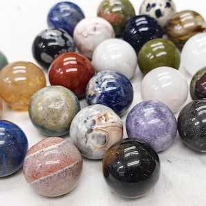 May include: A collection of polished gemstone spheres in various colors, including blue, green, orange, red, and white. The spheres have unique patterns and textures, reflecting light. These decorative spheres are ideal for display or collection.