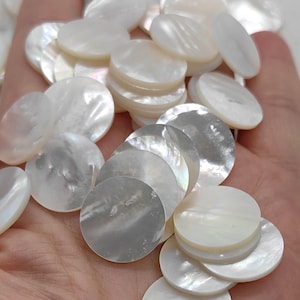 May include: A collection of iridescent, round, mother-of-pearl shell pieces. The white and silver-toned discs vary in size and are stacked and scattered, creating a shimmering effect. These natural shell components are ideal for crafting and jewelry making.