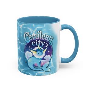 Puede incluir: Taza de cerámica blanca con interior y asa azules. La taza presenta un diseño con el texto "Cerulean City" y un personaje de dibujos animados en tonos azules, sobre un fondo acuático.