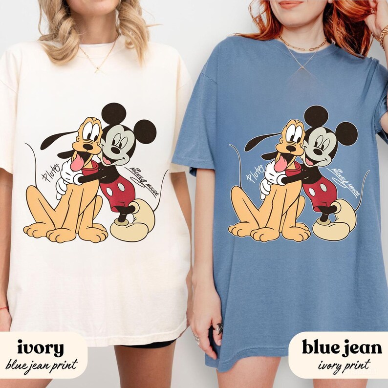 May include: Ivory and blue jean t-shirts featuring a graphic of Mickey Mouse hugging Pluto. The cartoon characters are in a warm embrace, with Pluto's tongue sticking out. The text "Mickey Mouse" is printed on the shirts.