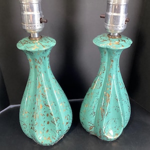 May include: A pair of turquoise ceramic lamp bases featuring a fluted, hourglass-shaped body with a metallic gold splatter pattern. Each lamp base is topped with a silver-toned metal socket fixture with a small black switch on the side.