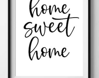 May include: A framed print with the words "home sweet home" in elegant black script on a white background. The print is in a black frame and is a digital download.