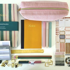 Op de afbeelding: Een briefpapier set met een gestreept A5-notitieboek, een mosterdgeel notitieboek, een roze corduroy etui, drie slanke pennen, een gouden liniaal, potloden, een pen, binderclips, hartvormige clips, een stickervel en een to-do lijstblok.