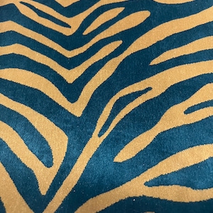 Könnte beinhalten: Nahaufnahme eines Stoffes mit Teal- und Gold-Zebramuster. Der Stoff weist kräftige, goldfarbene Streifen auf einem tiefen tealfarbenen Hintergrund auf. Das Muster ist ein sich wiederholendes Design, das eine auffällige visuelle Textur erzeugt. Der Stoff wirkt weich und plüschig.