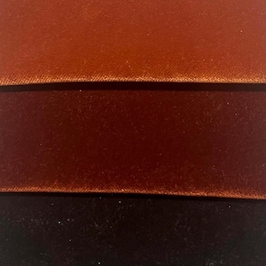 Puede incluir: Tres tiras horizontales de tela de terciopelo apiladas verticalmente. La tira superior es de un naranja cobre brillante, la tira central es de un rojo siena tostado profundo y la tira inferior es de color negro oscuro. Textura suave y brillante.