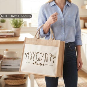 A woman is holding a large bag with a toothbrush and dental tools printed on it, standing in a kitchen.