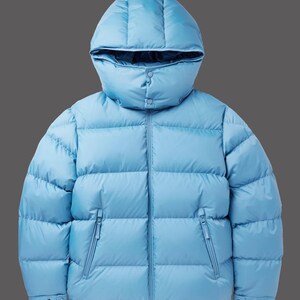 Puede incluir: Chaqueta acolchada azul claro con capucha. La chaqueta tiene un diseño acolchado, dos bolsillos con cremallera y un cierre de botón en la parte inferior. Para climas fríos.