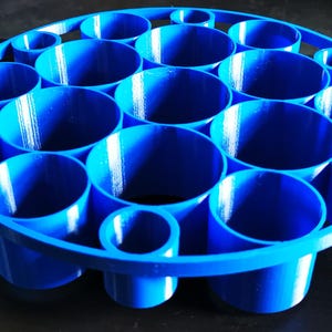 May include: A vibrant blue, circular organizer with multiple cylindrical compartments of varying sizes. The organizer is designed to hold and display items, with a sturdy base and a rim that defines the circular shape. The product is made of plastic.