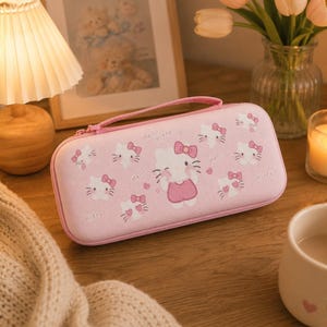 May include: A pink carrying case featuring a Hello Kitty design. The case has a zipper closure and a handle. The design includes multiple Hello Kitty faces and bows. The case is on a wooden surface.