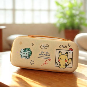 Peut inclure: Une trousse beige à fermeture éclair avec des personnages de dessins animés. La trousse a une poignée et est décorée avec un Bulbizarre, Pikachu, et du texte qui dit "Pika, Oh! You got a friend!" et du texte japonais. La trousse est sur une surface en bois.