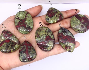 May include: Seven polished gemstones in various shapes, featuring a mix of green and deep red hues. The stones are held in a hand, showcasing their unique patterns and textures. These natural stones are ideal for jewelry making or collecting.