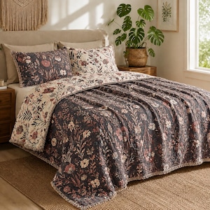 Op de afbeelding: Een bloemenquiltset in een slaapkamer. De quilt en kussenslopen hebben een donkergrijze achtergrond met crème- en mauve bloemmotieven. Het bed is opgemaakt met een bijpassende quilt en kussenslopen, wat zorgt voor een gecoördineerde en stijlvolle uitstraling.
