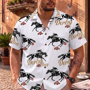 May include: White button-down shirt with a repeating pattern of black racehorses, riders, and red roses. The words "Derby Day" are printed in gold script across the shirt. The shirt has short sleeves and a pocket on the chest.