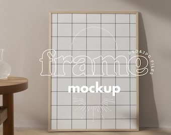 May include: A rectangular wooden frame mockup with a white grid pattern and the word "frame mockup" in white. The frame is leaning against a neutral-colored wall. The image includes a small wooden table and a glass vase.