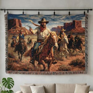 May include: A woven tapestry depicting a Western scene with cowboys on horseback in a desert landscape. The artwork features a cowboy in the foreground with a gun, leading a group of riders. The tapestry is displayed above a beige sofa.