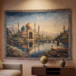 Puede incluir: Un gran tapiz que representa un paisaje detallado con un gran complejo de edificios, una masa de agua y una persona a caballo. El tapiz presenta una paleta de colores azules, dorados y verdes, con un borde con flecos.