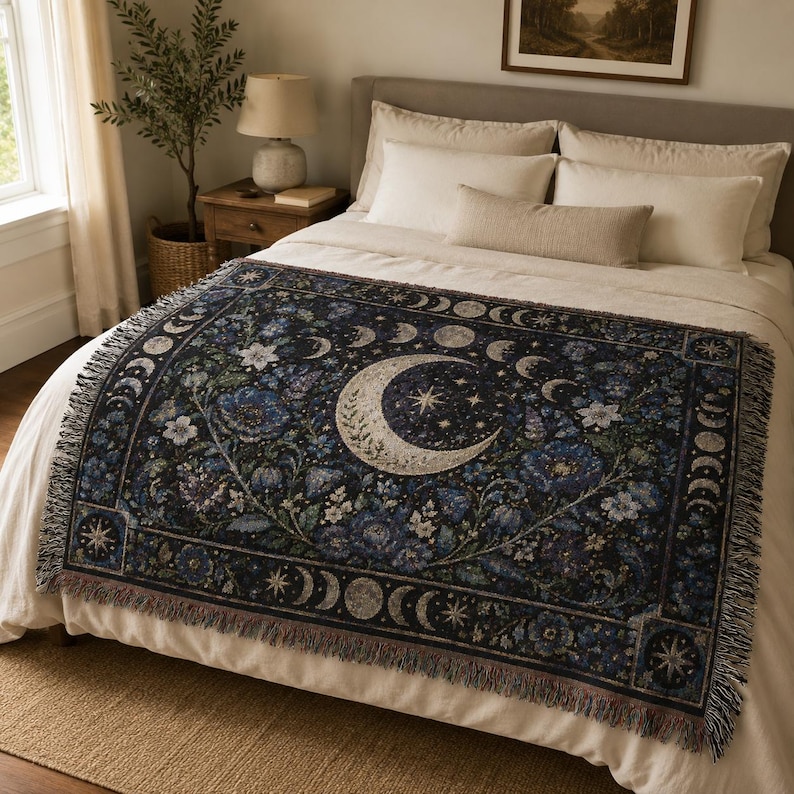 Horizontal woven blanket wall hanging with a large crescent moon, moon phase border, stars, deep blue flowers, white blossoms, dark botanical vines, ornate celestial frame, and fringed textile edges.