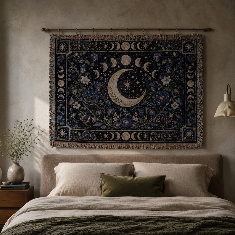 Horizontal woven blanket wall hanging with a large crescent moon, moon phase border, stars, deep blue flowers, white blossoms, dark botanical vines, ornate celestial frame, and fringed textile edges.