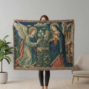 Horizontal woven blanket wall hanging featuring Archangel Gabriel kneeling before the Virgin Mary in an Annunciation scene, with lily flowers, halos, soft robes, garden landscape, old architecture, muted vintage colors, and fringed textile edges.