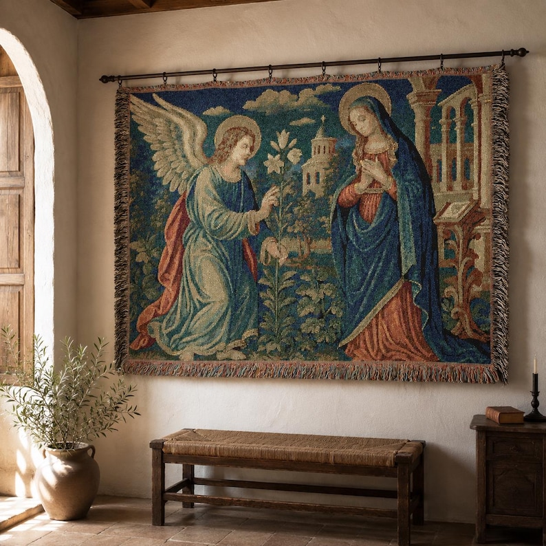 Horizontal woven blanket wall hanging featuring Archangel Gabriel kneeling before the Virgin Mary in an Annunciation scene, with lily flowers, halos, soft robes, garden landscape, old architecture, muted vintage colors, and fringed textile edges.