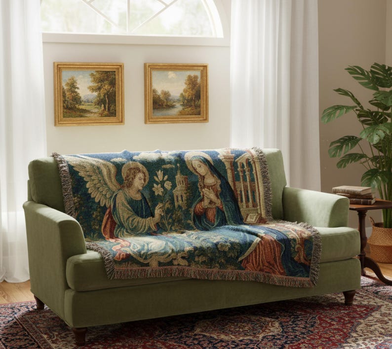 Horizontal woven blanket wall hanging featuring Archangel Gabriel kneeling before the Virgin Mary in an Annunciation scene, with lily flowers, halos, soft robes, garden landscape, old architecture, muted vintage colors, and fringed textile edges.