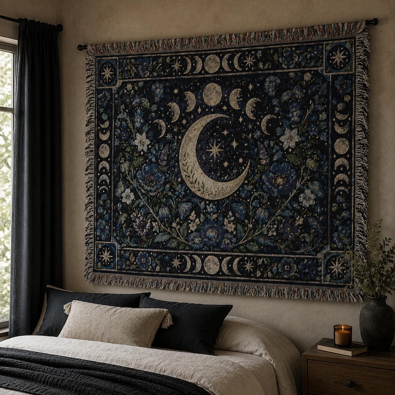 Horizontal woven blanket wall hanging with a large crescent moon, moon phase border, stars, deep blue flowers, white blossoms, dark botanical vines, ornate celestial frame, and fringed textile edges.