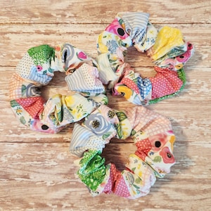 May include: Three colorful fabric scrunchies with floral and geometric patterns. The scrunchies are made of soft, stretchy fabric and are perfect for holding hair in place.