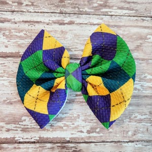 May include: A green, purple, and yellow plaid bow with a diamond pattern. The bow is made of fabric and has a textured surface.