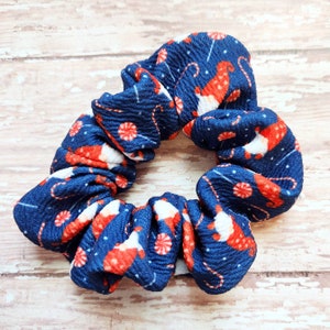 May include: A blue scrunchie with a white and red Christmas pattern featuring candy canes and gnomes.