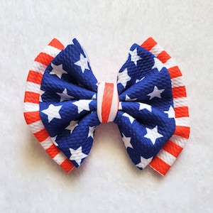 May include: A red, white, and blue bow with a star pattern. The bow is made of fabric and is perfect for adding a patriotic touch to any outfit.