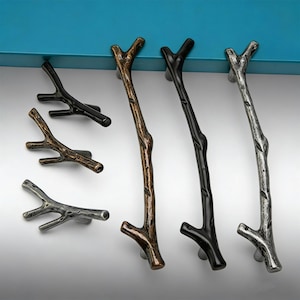 May include: A selection of branch-shaped cabinet handles in different finishes. The handles feature bronze, black, and silver colours, with a textured, natural look. These hardware pieces are designed to add a rustic or nature-inspired touch to furniture, such as drawers or cupboards.