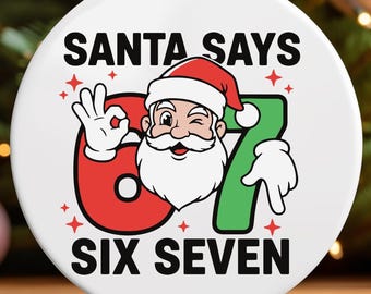 May include: A round white Christmas ornament with the text "SANTA SAYS 67 SIX SEVEN" and a cartoon Santa Claus illustration. The ornament has a red and green color scheme and is hanging from a natural twine string.