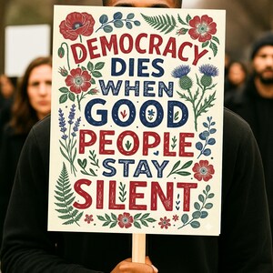 May include: A sign held by a person with the text "DEMOCRACY DIES WHEN GOOD PEOPLE STAY SILENT" in red and blue lettering, surrounded by floral illustrations. The sign is on a wooden stick.