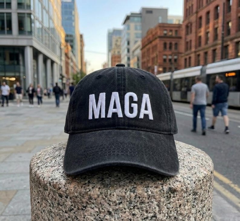 May include: A black baseball cap with a washed, distressed texture featuring the text MAGA embroidered in white capital letters across the front panel. The cap has a curved brim and a structured crown, showcasing a classic six-panel design.