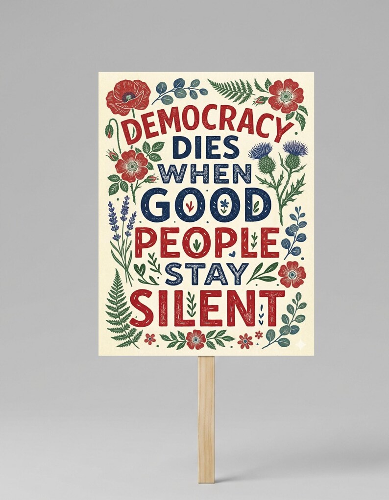 May include: A rectangular sign with the text "DEMOCRACY DIES WHEN GOOD PEOPLE STAY SILENT" in red and blue lettering. The sign is decorated with floral and botanical illustrations in red, green, and blue. It is mounted on a wooden stick.