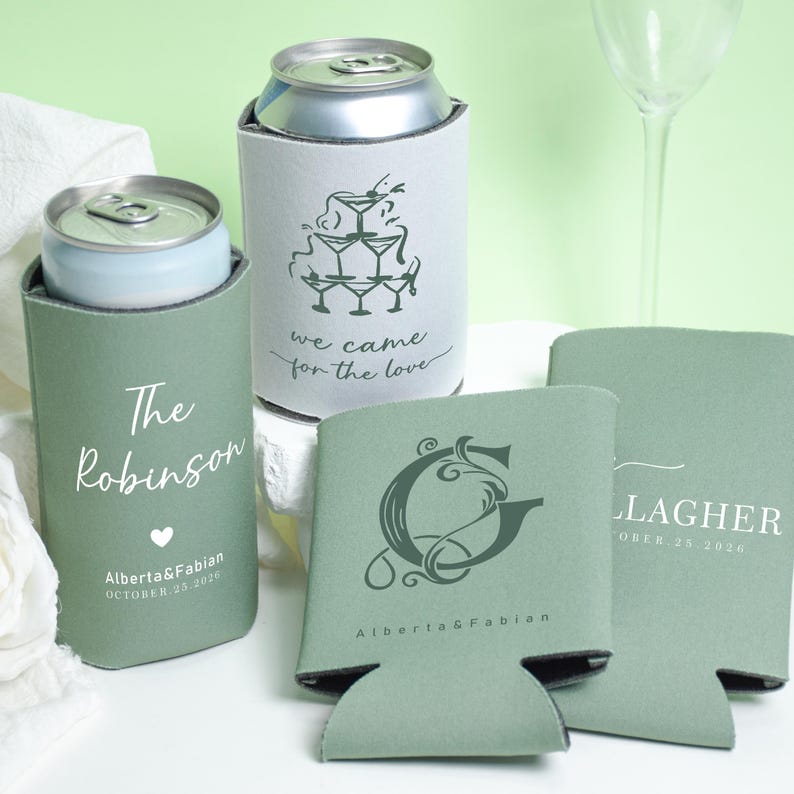 May include: Sage green can coolers with personalized text and designs. One cooler says "The Robinson" with a heart and date. Another says "we came for the love" with a martini glass design. Other coolers have initials and names.