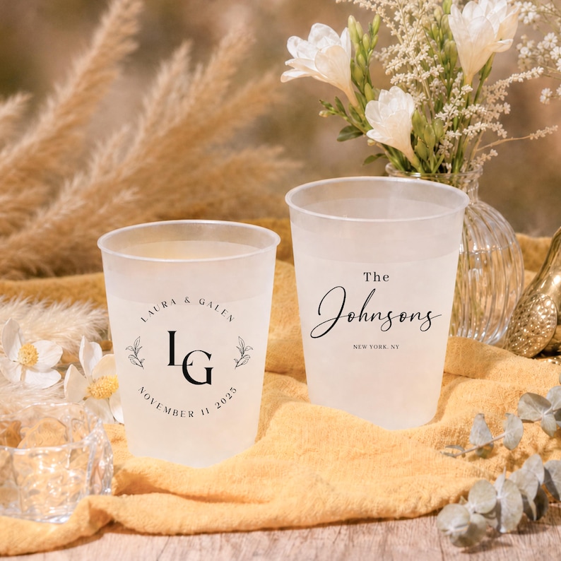 May include: Two frosted plastic cups with custom text for a wedding. One cup reads "Laura & Galen" with initials and a date. The other cup reads "The Johnsons" and "New York, NY".