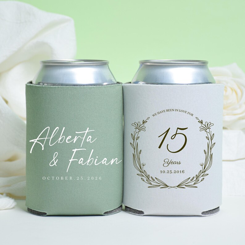 May include: Two can coolers, one sage green and one white. The green cooler has the names "Alberta & Fabian" and the date "OCTOBER 25 2026". The white cooler has the text "WE HAVE BEEN IN LOVE FOR 15 Years 10.25.2016" inside a floral wreath.