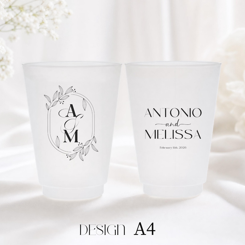 May include: Two frosted plastic cups with black text and designs. One cup features the initials "A" and "M" inside an oval with floral accents. The other cup has the names "Antonio and Melissa" and the date "February 11th, 2026". The design is labeled "DESIGN A4".